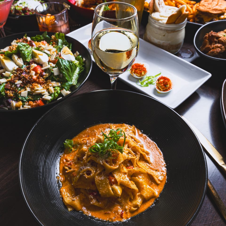 Southern-style pasta with red sauce, salad, deviled eggs, and white wine on a dark table.