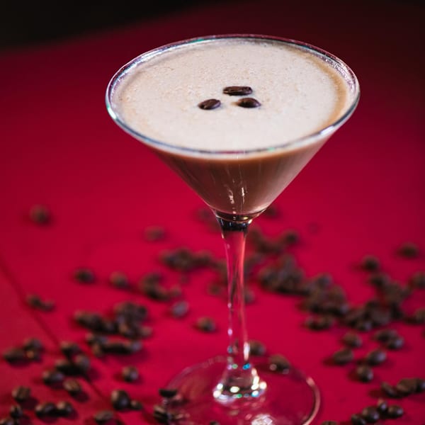 Espresso martini in a stemmed glass, garnished with three coffee beans on a red surface with scattered beans.